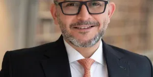 Mohamad Al-Dah, the new IStructE President 2025, in a dark suit, white shirt, glasses and an orange tie.