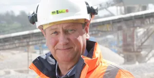A head and shoulders picture of Mike Phillips, CEO of the British Aggregates Association, wearing orange PPE and a white hard hat, in a quarry.