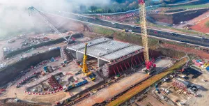 An aerial view of the A46 Kenilworth Bypass box structure under construction with a large yellow and red crawler crane and a smaller white telescopic crane and white crawler crane. Image: HS2.