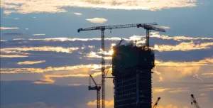 A High rise building under construction in silhouette with the sun setting behind it with three tower cranes