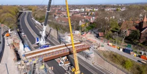 An aerial view of the new M67 St Annes Bridge under construction with a yellow crane on the near side of the bridge and a white crane on the far side.