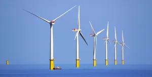 Six white and yellow wind turbines on a calm sea, part of the Walney Offshore Windfarm. Image: David Nixon / Creative Commons.