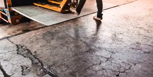 A man using a yellow trolly to unload a lorry onto a loading dock