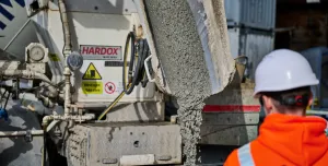 A man in orange PPE and a white hard hat watches low-carbon concrete being delivered for Holcim UK