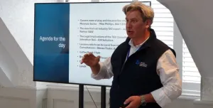 Mike Phillips, CEO British Aggregates Association, wearing a black, fleece gillet, open-necked white shirt and brown chinos, stands in front of a screen, speaking at the BAAs recent Landfill Tax consultation conference.