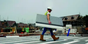 A man in PPE walks across new floor made from Milbank Concrete Products' GDeck, while carrying a panel of the lightweight flooring system.