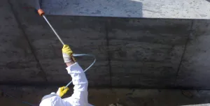 A man in white PPE Waterproofing underground sections of concrete with Vetrofluid using a low pressure pump.