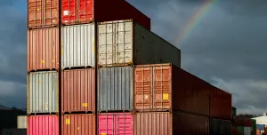 Multi-coloured containers stacked up in a yard with storm clouds and a rainbow in the background