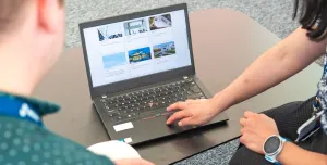 Two people look at a laptop screen which shows several photos and text related to sustainable construction