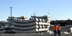 Two men in orange PPE stand next to a stack of precast concrete tunnel segments at the Western Harbour Tunnel Precasting facility in Emu Plains.