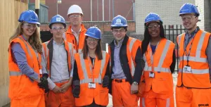 A group of students wearing orange PPE and blue hard hats stand outside a college of FE to celebrate the launch of the The new Construction Technical Excellence Colleges, which will train young people and career switchers in core trades including groundworks and bricklaying.