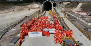 A large crowd of constructions workers in orange PPE stand by the entrance to the recently completed Chiltern Tunnel, HS2’s longest, which is now structurally complete following five years of construction. 