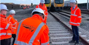 A group of people in Network Rail branded PPE inspect a concrete railway sleeper. The first-generation low-carbon concrete sleepers were installed by Concretene at GCRE in South Wales using 3.75 kg less cement per unit.
