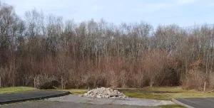 A dead-end road with a pile of illegally dumped concrete hardcore, with trees in the background.