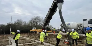 construction workers in yellow PPE lay concrete that's being delivered via chute from a concrete mixer