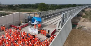 A large group of orange-clad PPE wearing construction workers gather at one end of the colne Valley Viaduct. Over 3,600 m³ of concrete was poured to form the kerb along the 3.4 km Colne Valley Viaduct – now structurally complete.