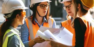 In the warm glow of the afternoon sun, a team of construction professionals gather closely, passionately engaged in a project discussion. Clad in safety helmets and high-visibility vests, they exchange ideas over blueprints, their collaboration a testament to the intricate planning that underpins successful infrastructure projects. Each individual's focused expression underscores the importance of each decision in the grand tapestry of urban development.