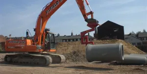 An orange excavator lifts a concrete pipe
