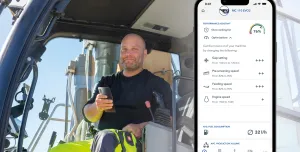 A PPE clad construction worker sits in a machine cab holding a mobile, with a screen shot of the mobile using Kleemann’s SPECTIVE CONNECT app, which now enables remote control and monitoring of crushing and screening equipment, on the right of the picture.