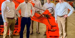 Five men dressed in smart shirts and trousers stand around a large red excavator arm