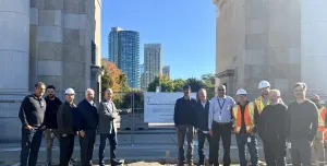 A group of people in business wear and PPE celebrate the use of Bio Graphene Solutions’ graphene-enhanced low-carbon concrete beneath Toronto’s historic Princes’ Gates at Exhibition Place.