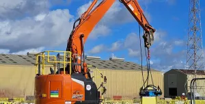 An orange, zero tail-swing midi excavator lifts a pile cropper on a construction site
