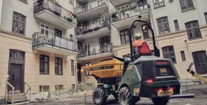 A yellow site dumper being driven in front of an urban construction site