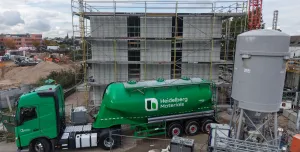A green, Heidelberg Materials' cement truck in front of an under construction house