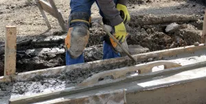 A construction worker using a trowel to help lay concrete foundations
