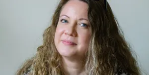 A head shot of Laila Morris, newly appointed practice director at Betts Associates, with long curly hair, a checked top and glasses on her head