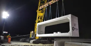 A yellow Kobelco crawler crane lifts a precast, rectangular concrete element
