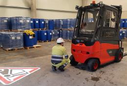 A man in a factory crouching down in front of a forklift