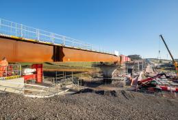 A steel bridge deck being slid into position with a crane in the background