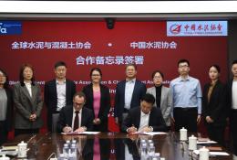 Several people standing around a table looking at two men signing a document