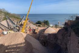 A picture of a yellow crane in a quarry with the sea in the background