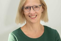 A head and shoulders picture of a blond haired woman in glasses and a green jumper