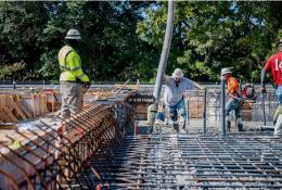 Four US construction workers in bright tshirts and PPE pour concrete