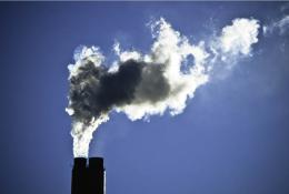 The top of a smoking industrial chimney with black and white smoke billowing from the top