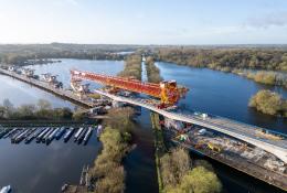 An aerial shot of a red bridge launcher crossing a river and canal