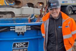 A man in orange PPE standing in front of a blue metal cylinder