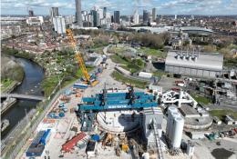An aerial shot of a construction site with a yellow crawler crane and a large blue gantry crane