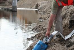 A man in red PPE holds a dewatering pump in water