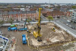 An aerial photo of a construction site with blue concrete mixers and concrete pump, and a yellow foundation rig