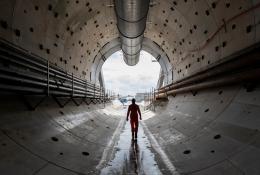 A man in yellow PPE silhouetted against the entrace to a concrete lined tunnel 