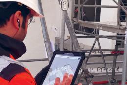 A man in orange PPE looking at a tablet screen