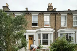 A man in shorts working in the front garden of a victorian terrace house