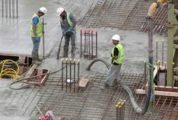 Three UK construction workers in PPE using a concrete pump to place concrete