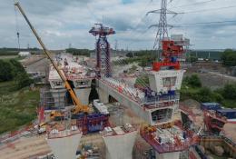 An aerial picture of a viaduct under construction with a yellow crane and red formwork.