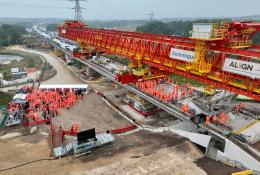 Two large groups of people in orange PPE standing on an under construction bridge deck
