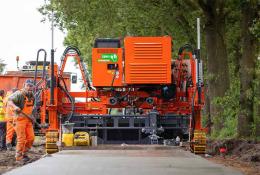 Men in orange PPE working on a raod paving project with an electric slipform paver